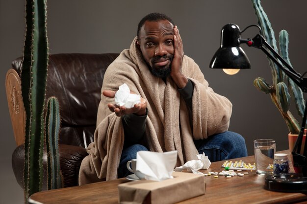 Young africanamerican man wrapped in a plaid looks sick ill has terrible headache sitting at home