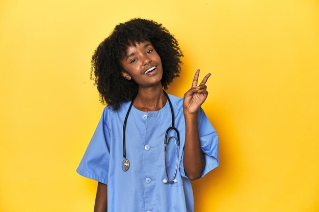 젊은 아프리카계 미국인 간호사가 스튜디오에서 노란색 배경으로 즐겁고 무관심합니다.