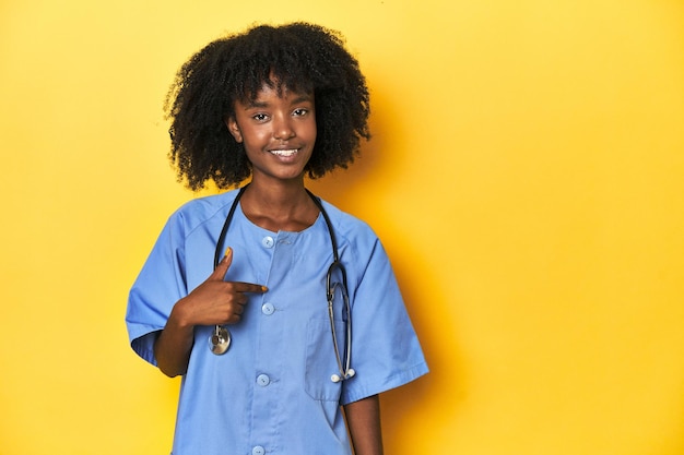 黄色い背景の人が手で指さしているスタジオの若いアフリカ系アメリカ人の看護師