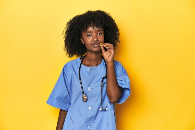 Young AfricanAmerican nurse in studio with yellow background with fingers on lips keeping a secret