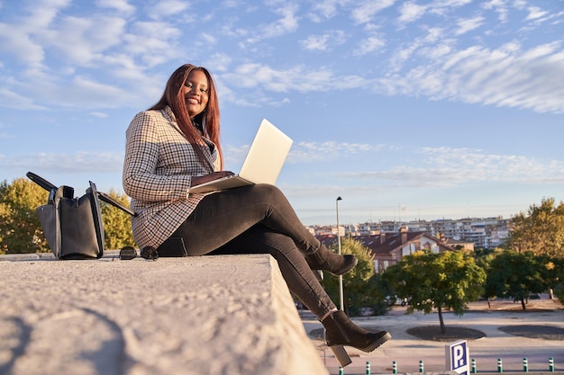 Young AfricanAmerican woman sitting outdoors working on laptop computer