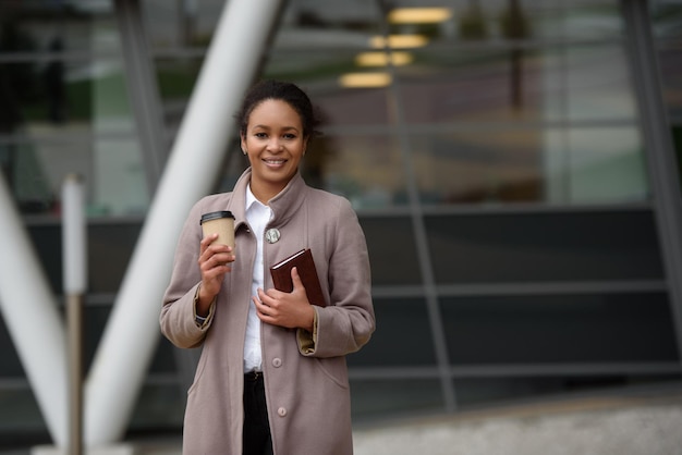 Молодая афроамериканская деловая женщина с блокнотом и кофе на улице
