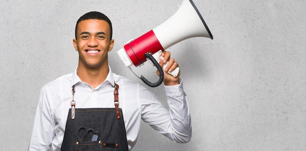 Young afro american barber man holding a megaphone on textured wall