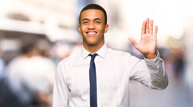 Young afro american businessman saluting with hand with happy expression in the city