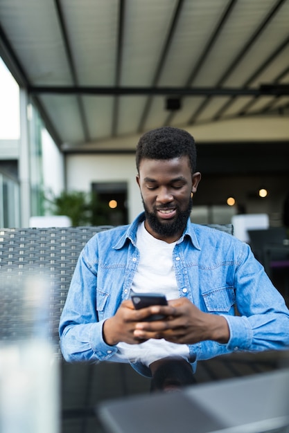 Young Afro American businessman with glasses and laptop sitting in cafe bar and use cell phone.