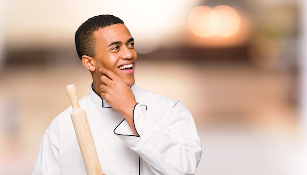 Young afro american chef man thinking an idea while scratching head on unfocused background