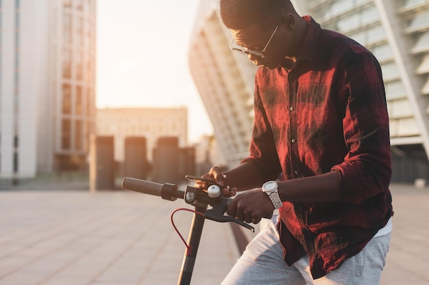 Young afro american guy renting an electric scooter on the street a student scans the eco transport