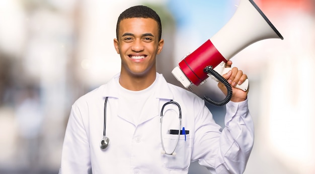 Young afro american man doctor holding a megaphone at outdoors