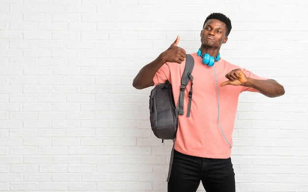 Young afro american man student making good-bad sign. Undecided person between yes or not