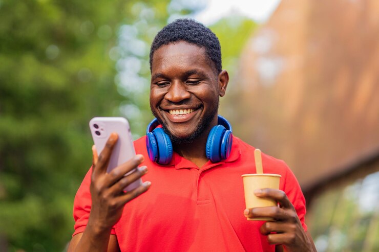 Young afro american man with headphones on neck using smartphone in summer park