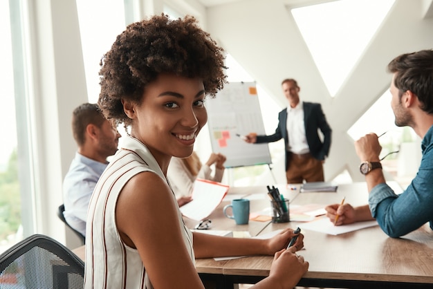 Young afro american woman is looking at camera and smiling while her boss standing near