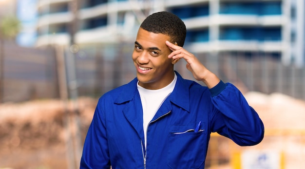 Young afro american worker man saluting with hand in a construction site