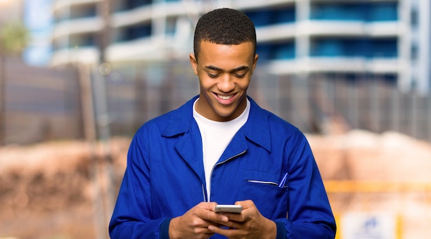 Молодой афро американский рабочий человек, отправив сообщение с мобильного телефона на строительной площадке
