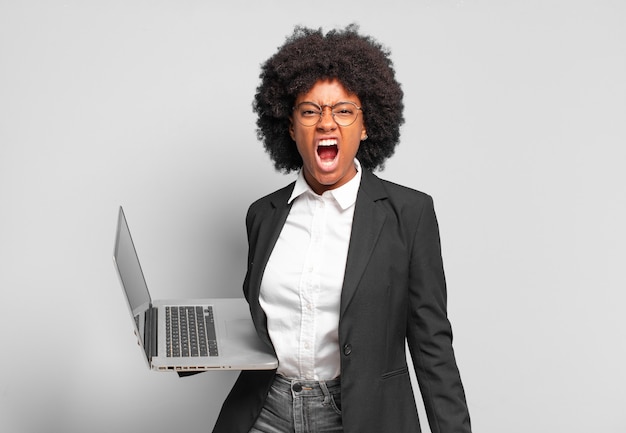 Young afro businesswoman shouting aggressively, looking very angry, frustrated, outraged or annoyed, screaming no. business