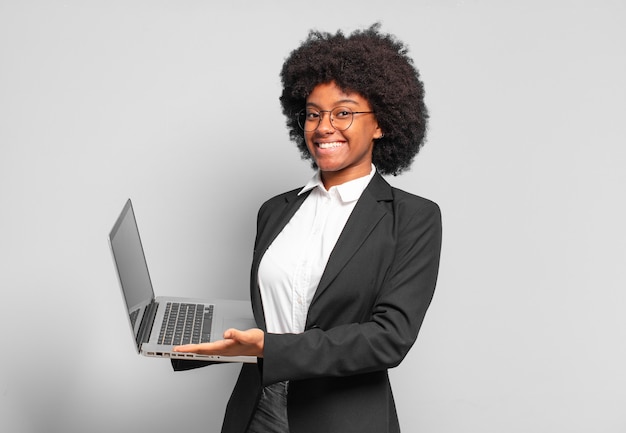 Young afro businesswoman smiling cheerfully, feeling happy and showing a concept in copy space with palm of hand. business concept