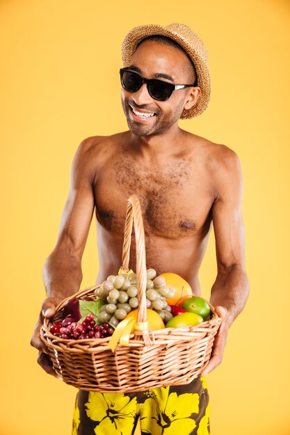 Young afro man holding fruit basket isolated on a orange wall