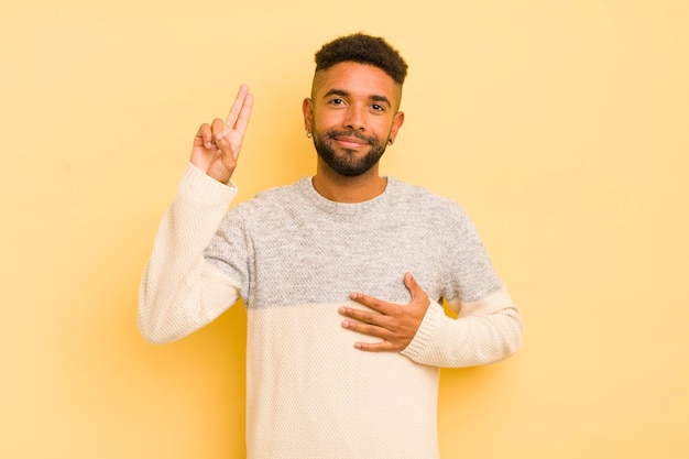 Young afro man looking happy confident and trustworthy smiling and showing victory sign with a positive attitude