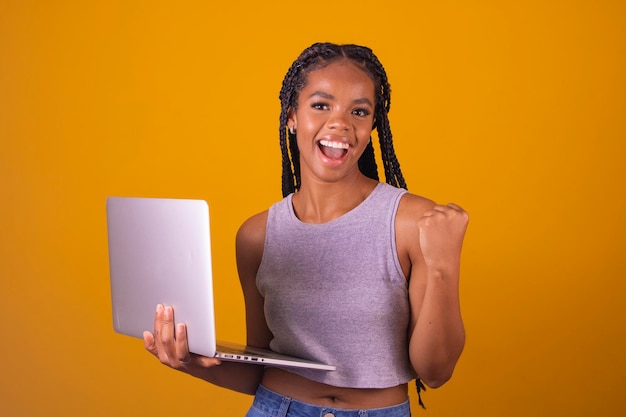 Young afro man with laptop on color background celebrating