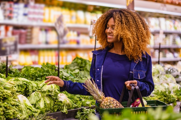 Молодая афро женщина покупает овощи в супермаркете.