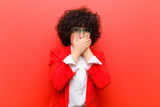 Foto giovane donna afro che copre la bocca con le mani con un'espressione scioccata e sorpresa, mantenendo un segreto o dicendo oops