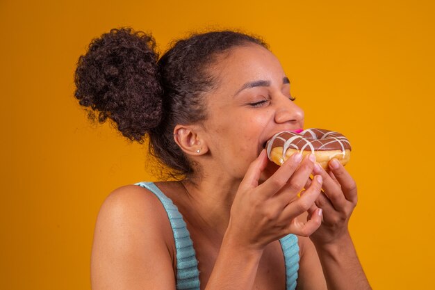 Young afro woman eating delicious chocolate donuts.