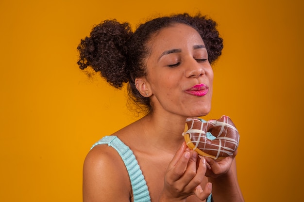 Young afro woman eating delicious chocolate donuts.