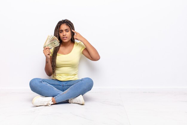 Young afro woman feeling confused and puzzled, showing you are insane, crazy or out of your mind. money concept