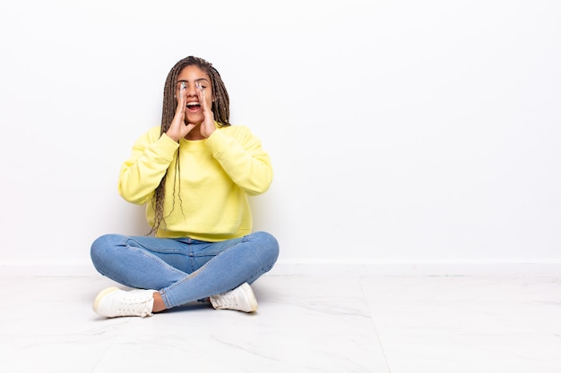 Young afro woman feeling happy, excited and positive, giving a big shout out with hands next to mouth, calling out