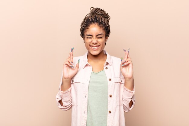 Young afro woman feeling nervous and hopeful, crossing fingers, praying and hoping for good luck