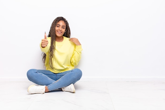 Young afro woman feeling proud, carefree, confident and happy, smiling positively with thumbs up