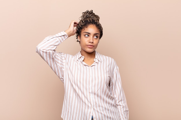 Young afro woman feeling puzzled and confused, scratching head and looking to the side