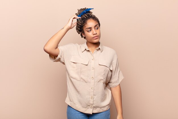 Young afro woman feeling puzzled and confused, scratching head and looking to the side