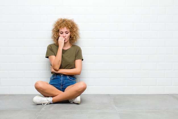 Young afro woman feeling serious, thoughtful and concerned, staring sideways with hand pressed against chin sitting on a floor