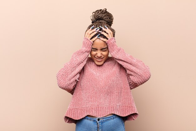 Young afro woman feeling stressed and frustrated, raising hands to head, feeling tired, unhappy and with migraine