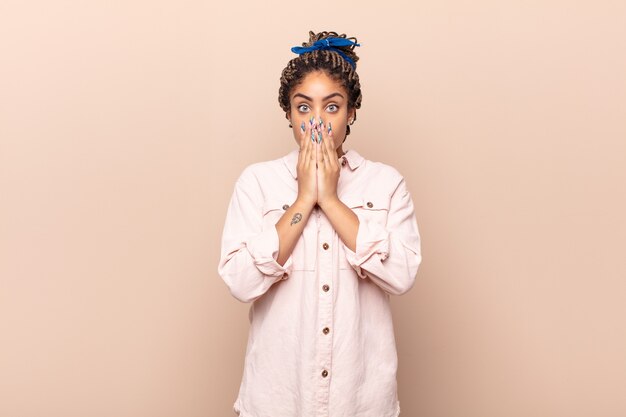 Foto giovane donna afro che si sente preoccupata, sconvolta e spaventata, coprendosi la bocca con le mani, sembrando ansiosa e avendo incasinato