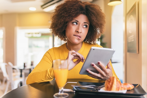 Young afro woman having a breakfast at cafe. She is drinking an orange juice