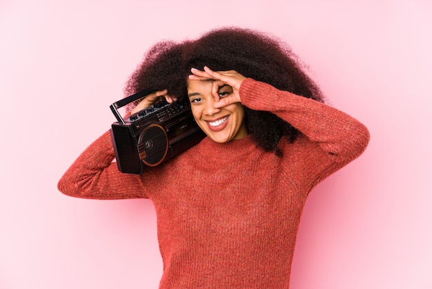 La giovane donna afro che tiene un cassete ha isolato eccitato mantenendo il gesto giusto sull'occhio.