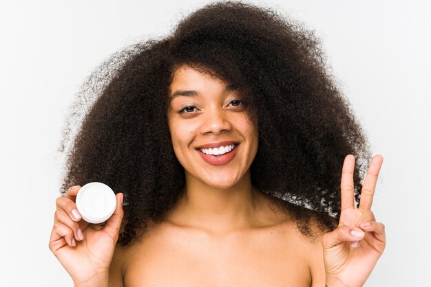 La giovane donna afro che tiene una crema idratante ha isolato la mostra del numero due con le dita.