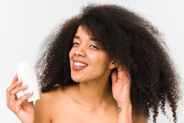 Young afro woman holding a moisturizer isolated trying to listening a gossip.