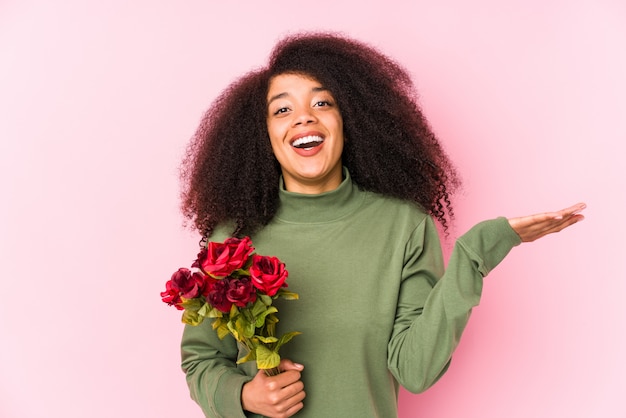 Young afro woman holding a roses isolated. Young afro woman holding a roses receiving a pleasant surprise, excited and raising hands.