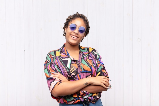 Young afro woman laughing happily with arms crossed, with a relaxed, positive and satisfied pose