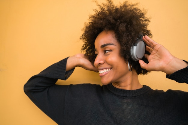 Молодая афро женщина слушая музыку с наушниками.