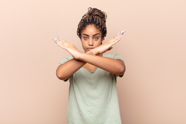 young afro woman looking annoyed and sick of your attitude, saying enough! hands crossed up front, telling you to stop