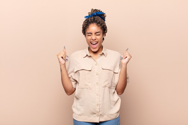 Young afro woman looking extremely happy and surprised, celebrating success, shouting and jumping