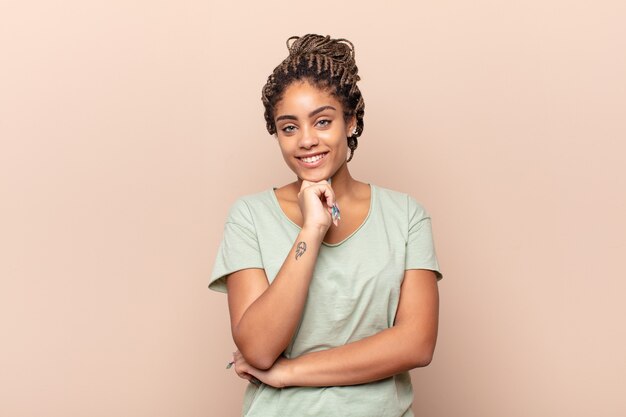 Young afro woman looking happy and smiling with hand on chin