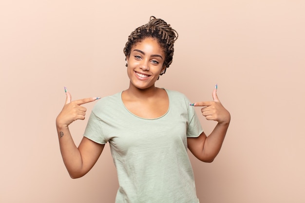 Young afro woman looking proud, arrogant, happy, surprised and satisfied, pointing to self, feeling like a winner