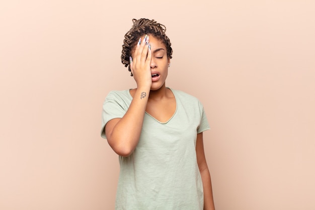 Foto giovane donna afro che sembra assonnata, annoiata e che sbadiglia, con un mal di testa e una mano che copre metà del viso