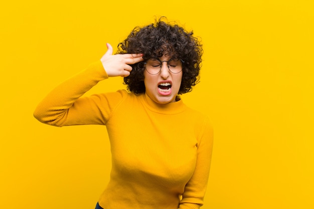 Young afro woman looking unhappy and stressed, suicide gesture making gun sign with hand, pointing to head