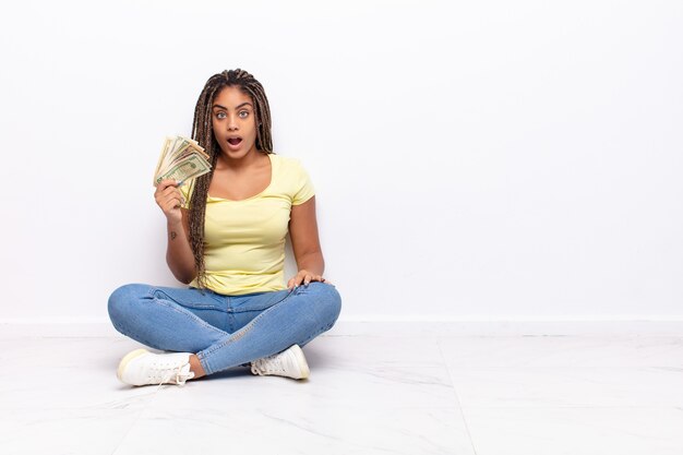 Young afro woman looking very shocked or surprised, staring with open mouth saying wow. money concept