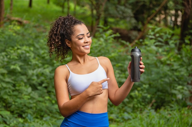 Young afro woman in the park holding a bottle of water.